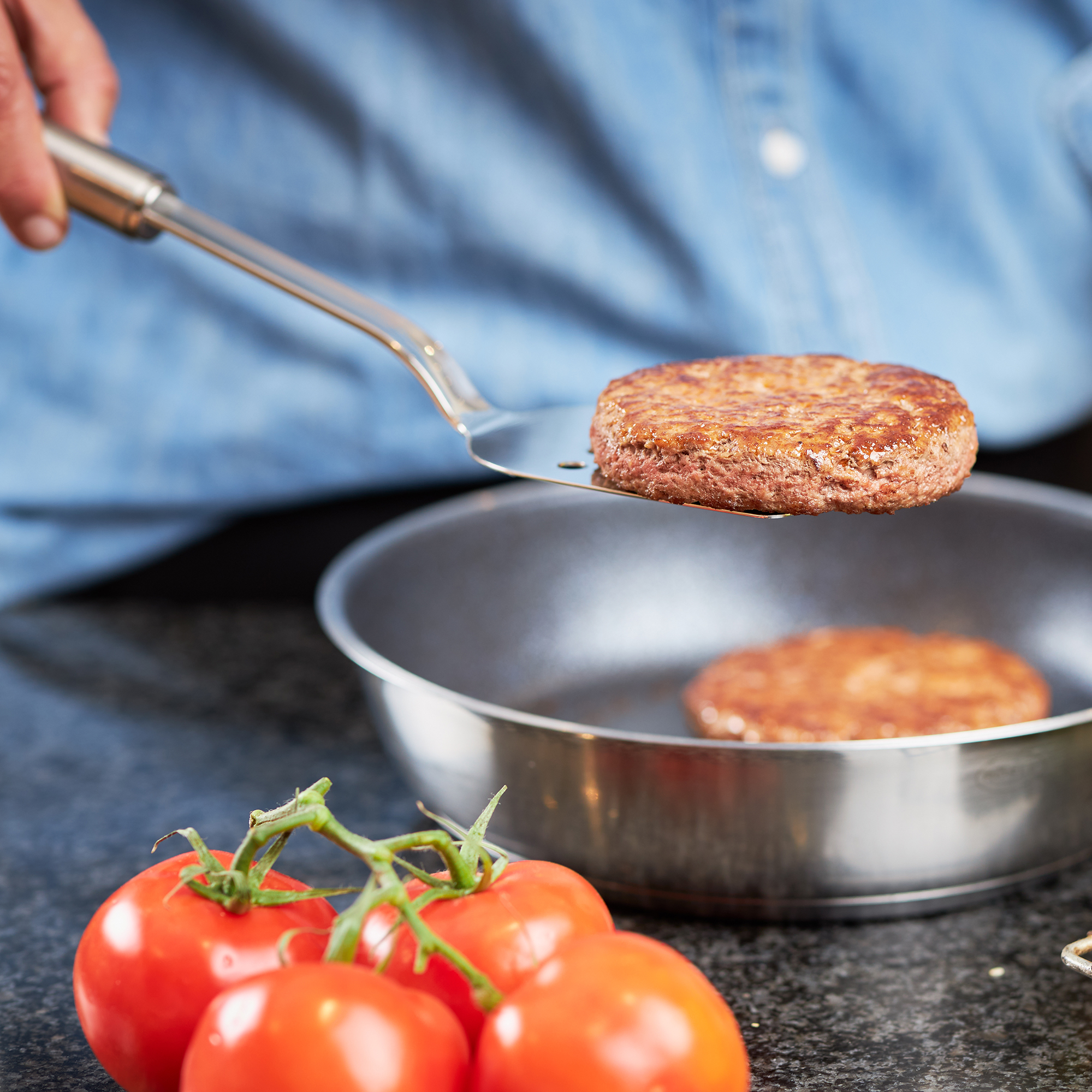 RÖSLE pan shovel turning a roast Stainless steel pan scoop, turning a roast in a pan, with fresh tomatoes in the foreground.