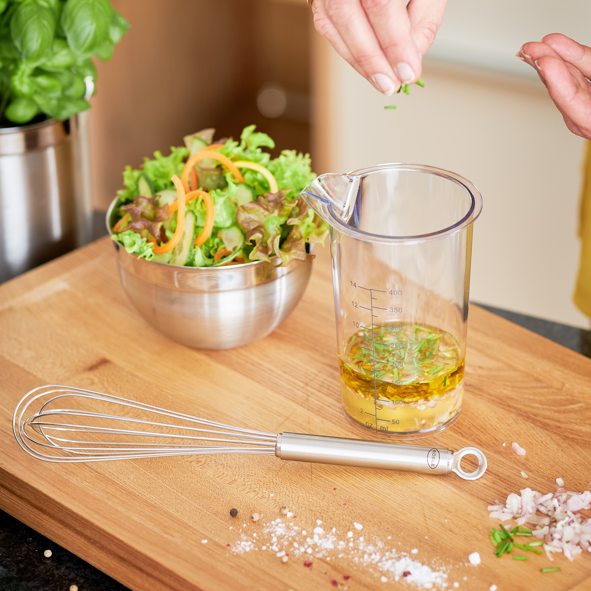 RÖSLE Messbecher mit Dressing und frischen Kräutern Messbecher aus Glas mit Dressing, frische Kräuter werden hinzugefügt, im Hintergrund eine...