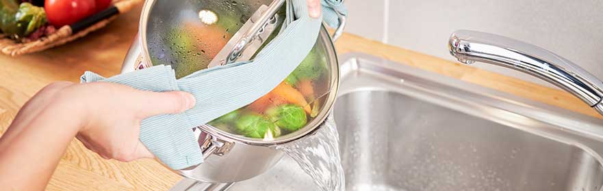 RÖSLE Exquisite Kochtopf beim Entleeren Exquisite Kochtopf wird über eine Spüle geleert, während Gemüse im Topf sichtbar ist.