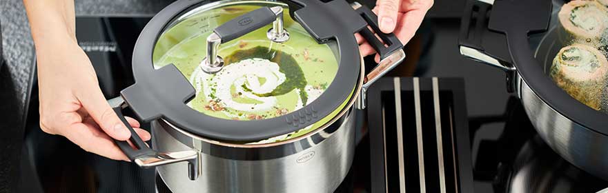 SILENCE PRO Silence Pro stainless steel cooking pot with glass lid held by one person while a green soup...