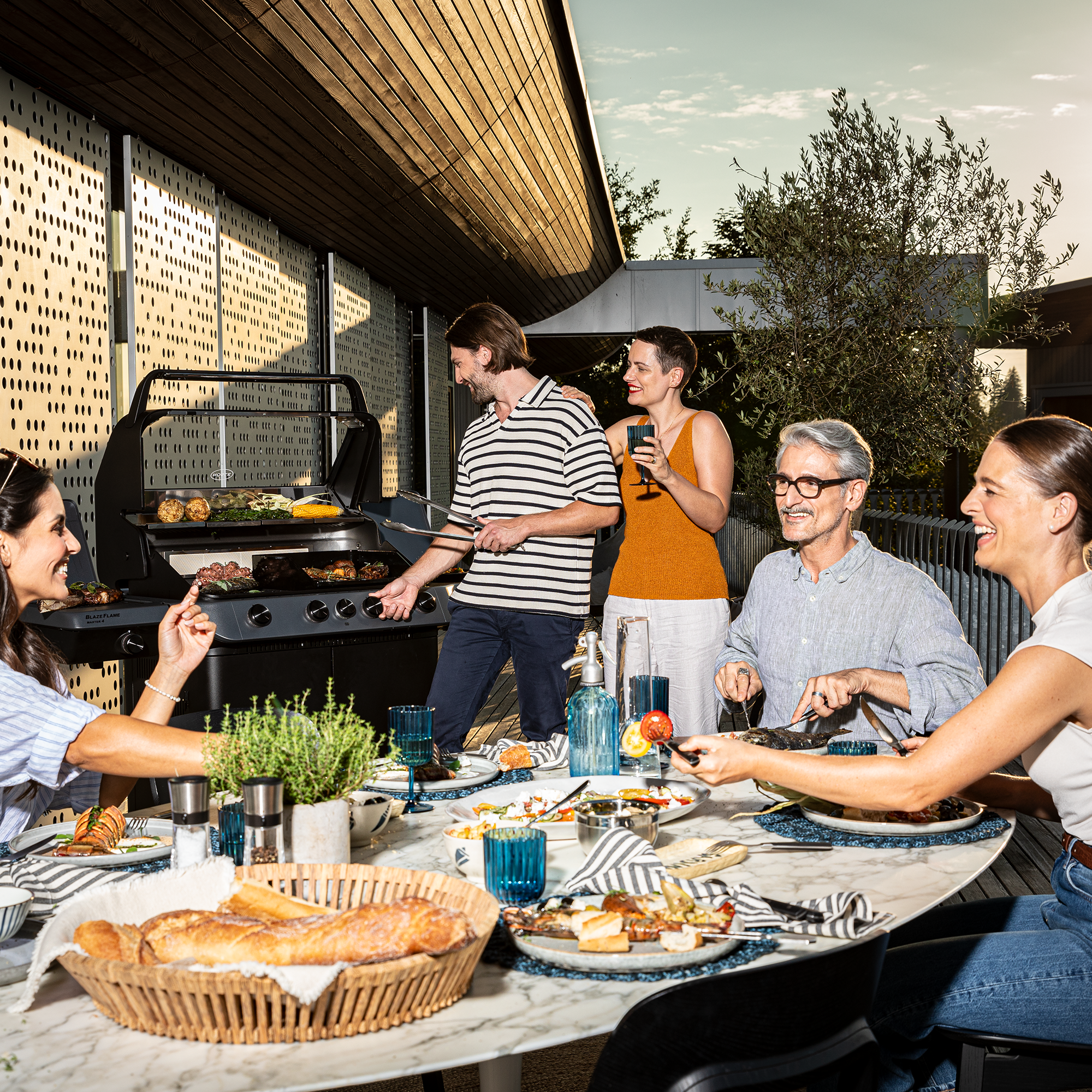 Grillabend mit RÖSLE Grill Grillabend mit Freunden, Grill im Hintergrund, Tisch mit verschiedenen Speisen und Getränken,...