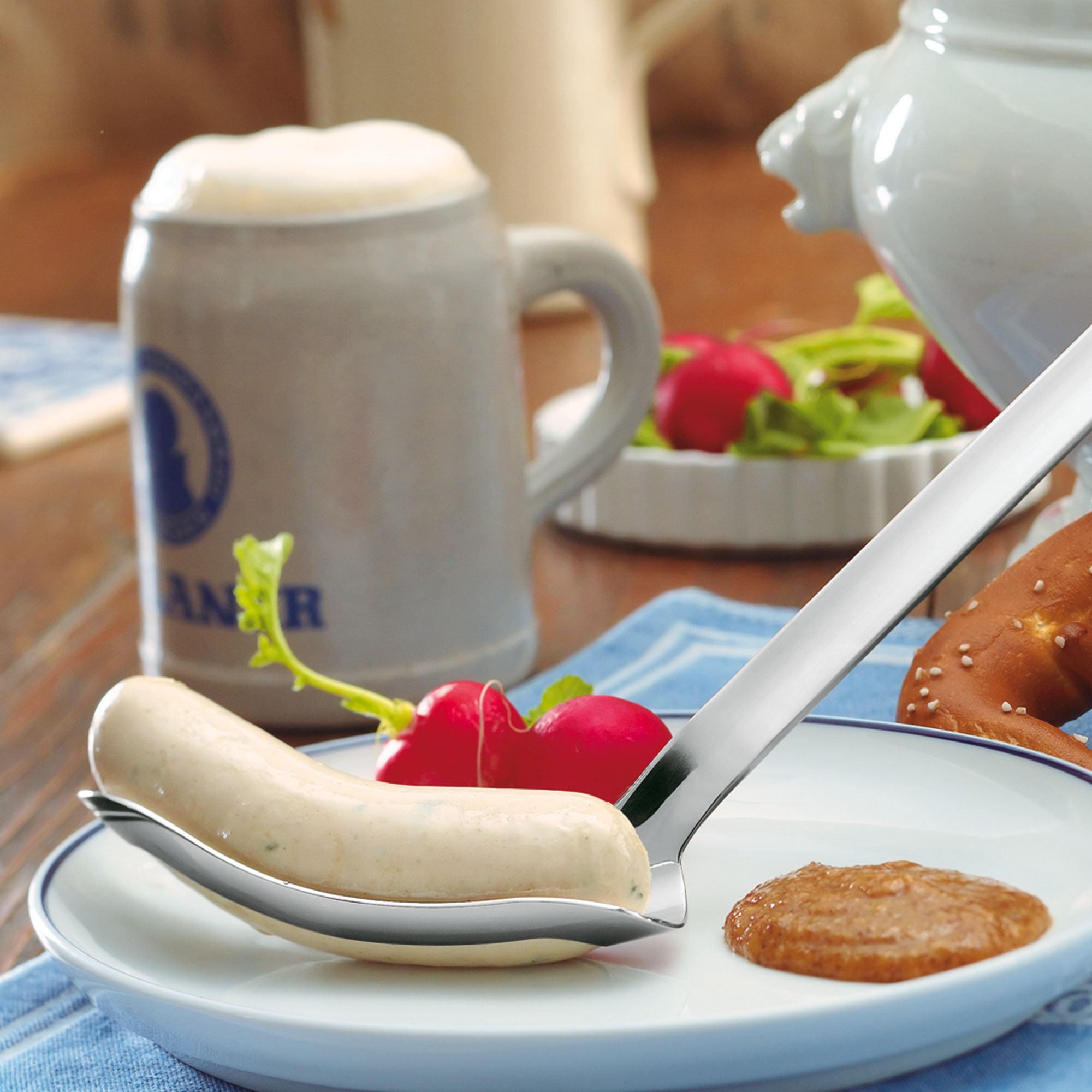 RÖSLE Weißwurstheber mit Weißwurst und Beilagen Weißwurstheber aus Edelstahl mit einer Weißwurst, Senf und Radieschen auf einem Teller.