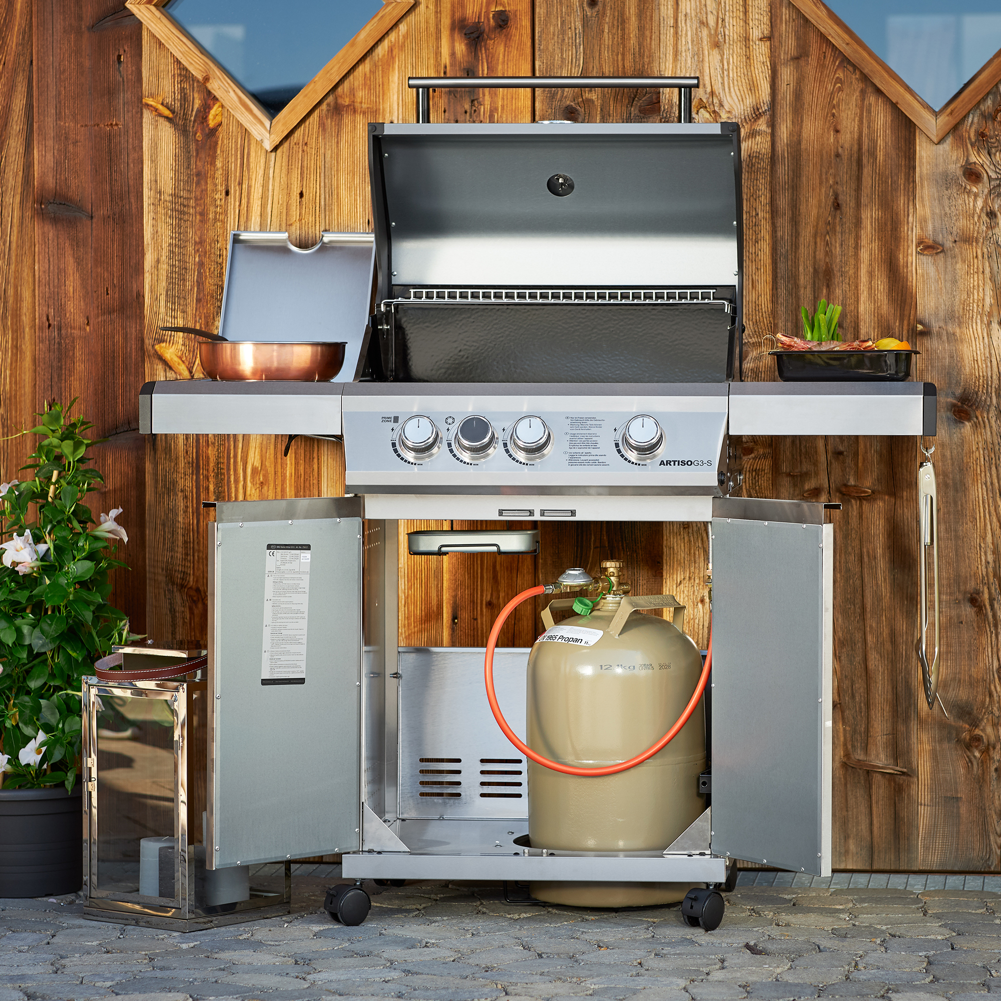RÖSLE Gasgrill Artiso G3-S Gasgrill BBQ Station Artiso G3-S aus Edelstahl mit geöffnetem Deckel, Gasflasche im Unterschrank.