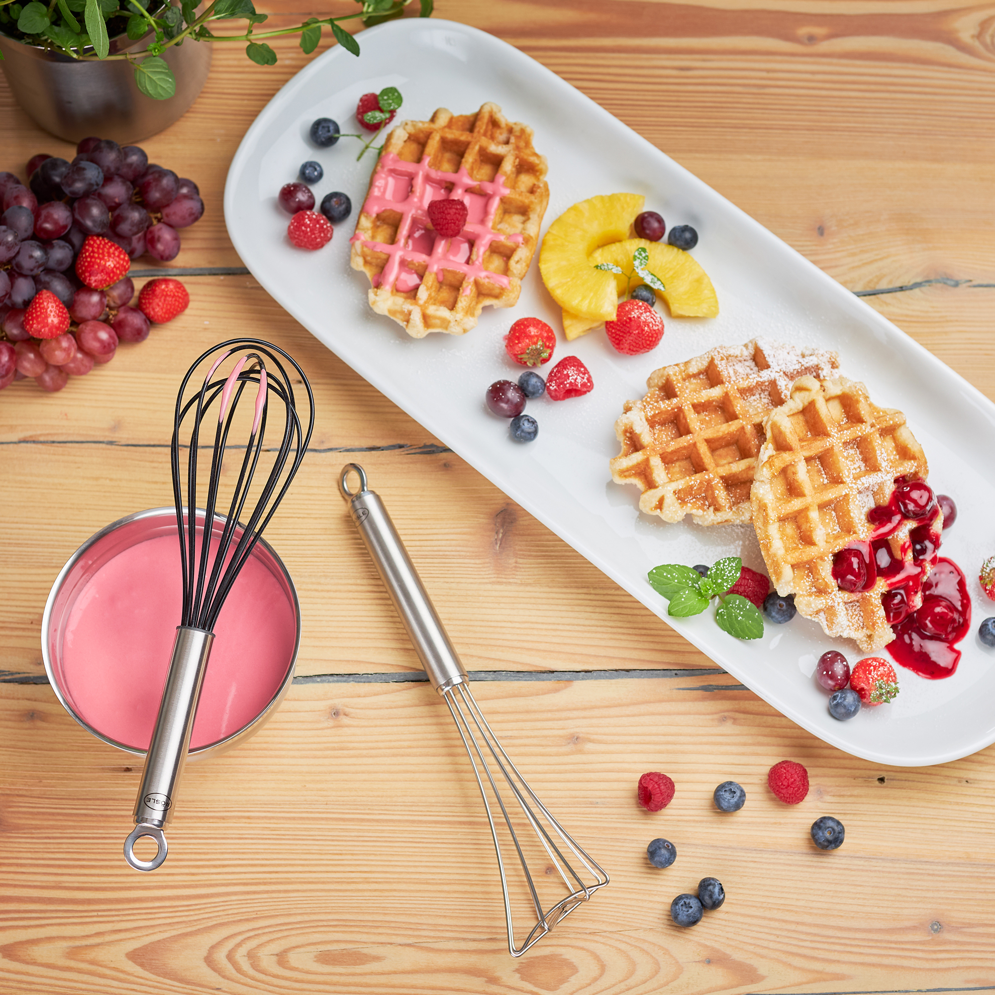 RÖSLE Gourmetbesen und Waffeln Gourmetbesen aus Edelstahl, 27 cm, neben Waffeln und frischem Obst auf einem weißen Teller.