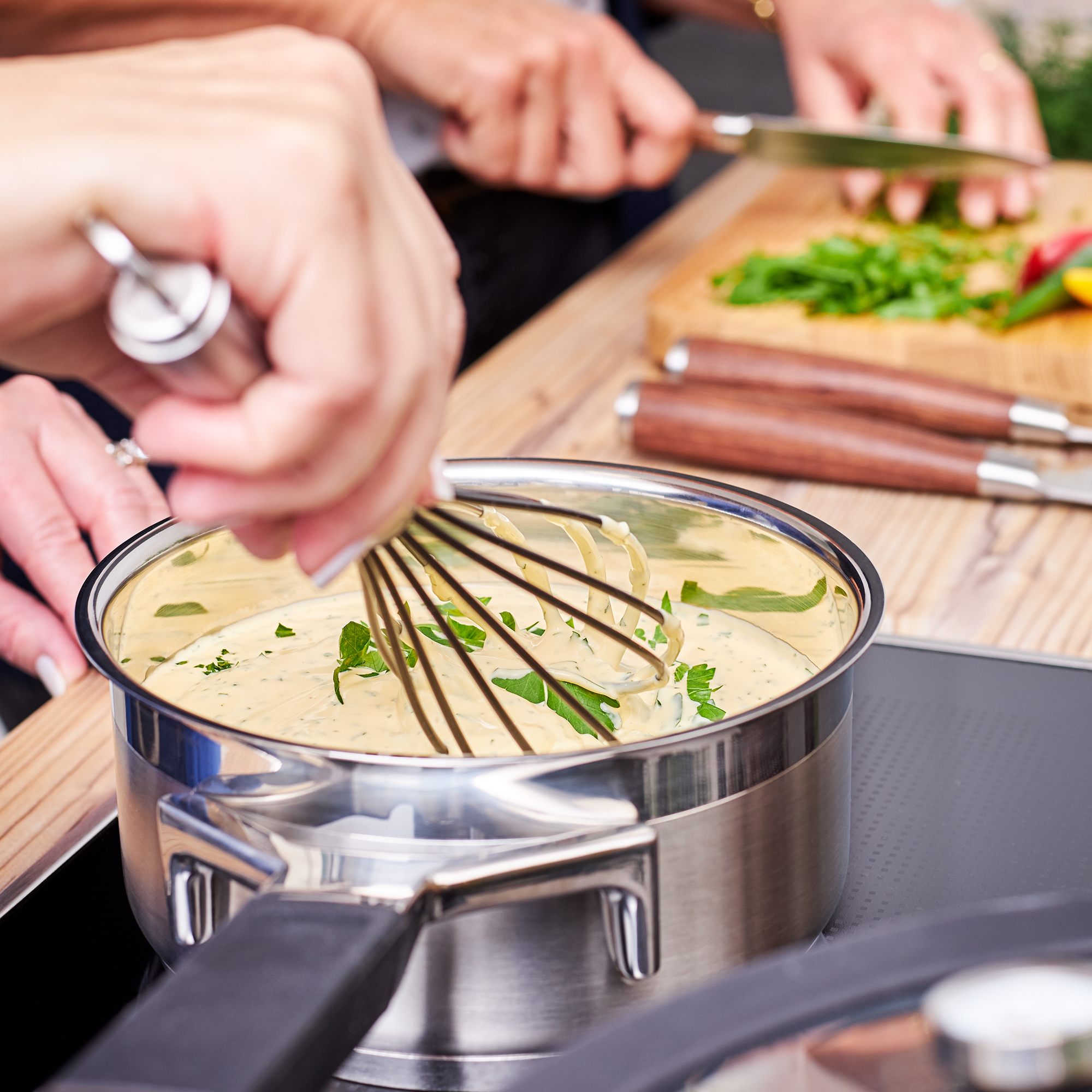 RÖSLE silicone whisk in action Silicone whisk in a stainless steel pan with a creamy sauce and fresh herbs, hands in the...