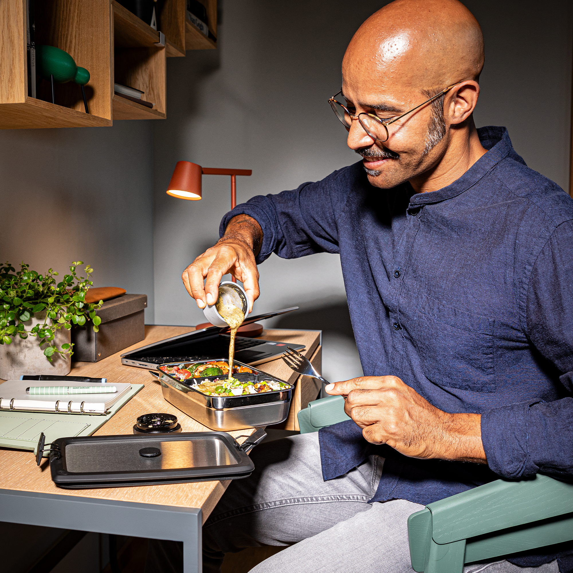 Mann mit RÖSLE Flexx2go Lunchbox Flexx2go 1,0l Lunchbox aus Edelstahl, ein Mann gießt Dressing über einen Salat am Schreibtisch.