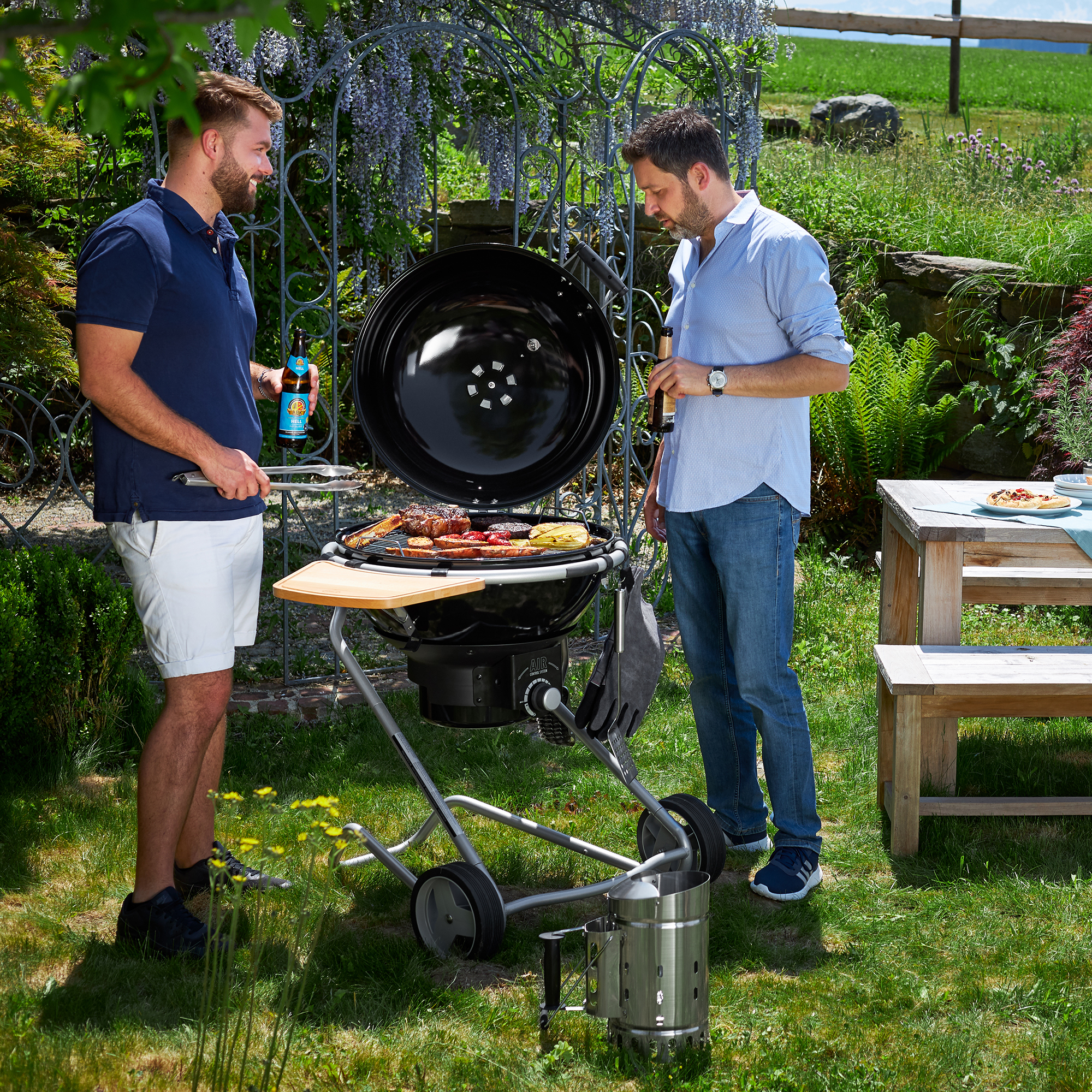 Zwei Männer beim Grillen mit RÖSLE Anzündkamin Zwei Männer grillen im Freien mit einem Edelstahl-Anzündkamin und einem Grill.