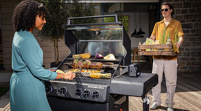 Gasgrill Serie ALLFLAME Frau grillt auf dem ALLFLAME Gasgrill, während der Mann Getränke in einer Holzkiste bringt.