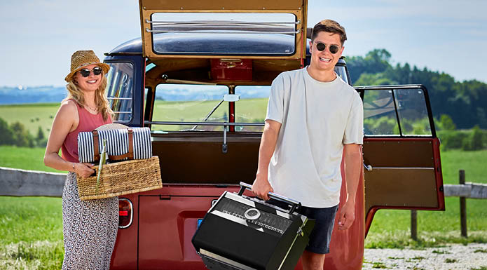 Man carrying portable gas grill and woman picnic basket