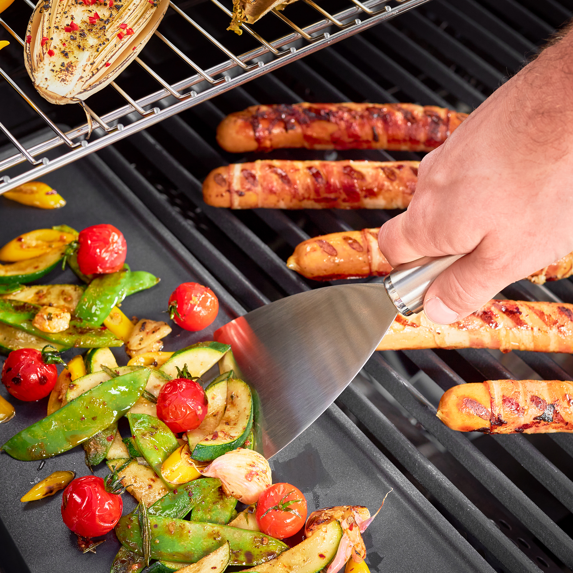 RÖSLE barbecue spatula with barbecue food Grill spatula in use, for turning vegetables and sausages on the grill grate.
