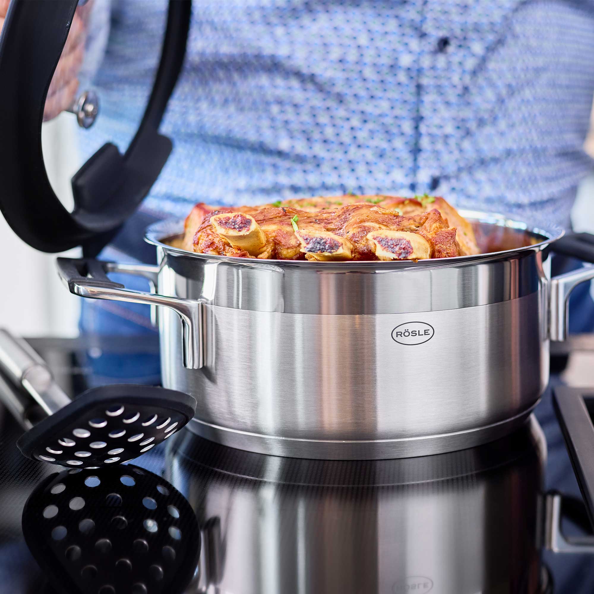 RÖSLE Bratentopf Silence PRO 20 cm Bratentopf Silence PRO, 20 cm, aus Edelstahl, mit Fleischstücken und Deckel, auf einem Herd.
