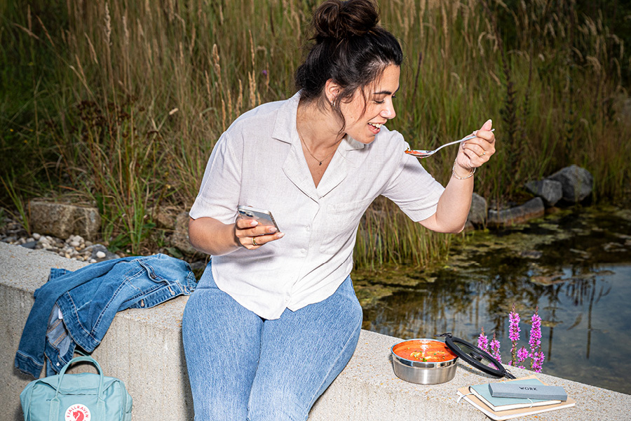 Studentin isst Suppe aus FLEXX 2GO Dose im Campus-Außenbereich