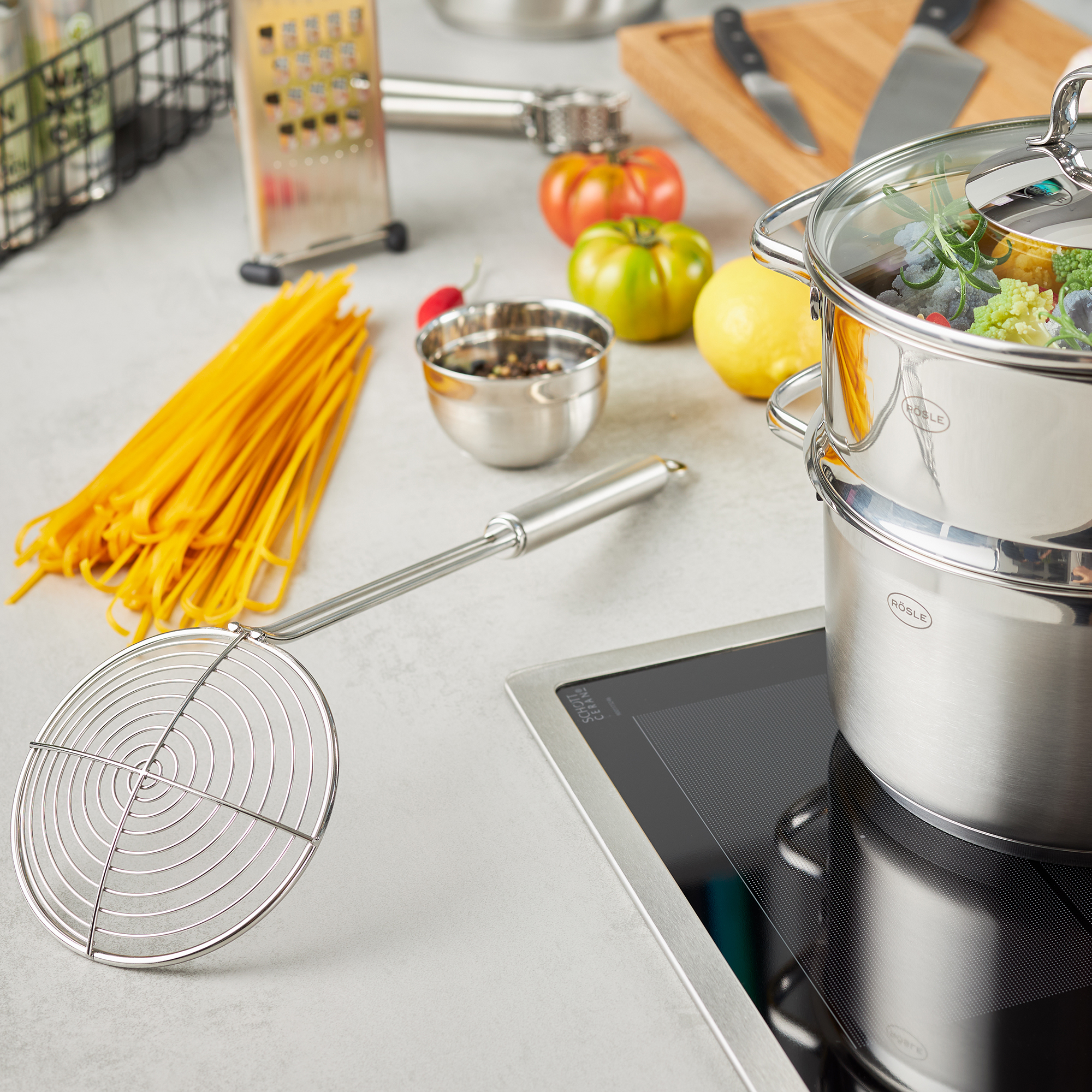 RÖSLE Seihlöfel 14 cm Stainless steel colander, 14 cm, lies next to a pot of vegetables and spaghetti on a work...