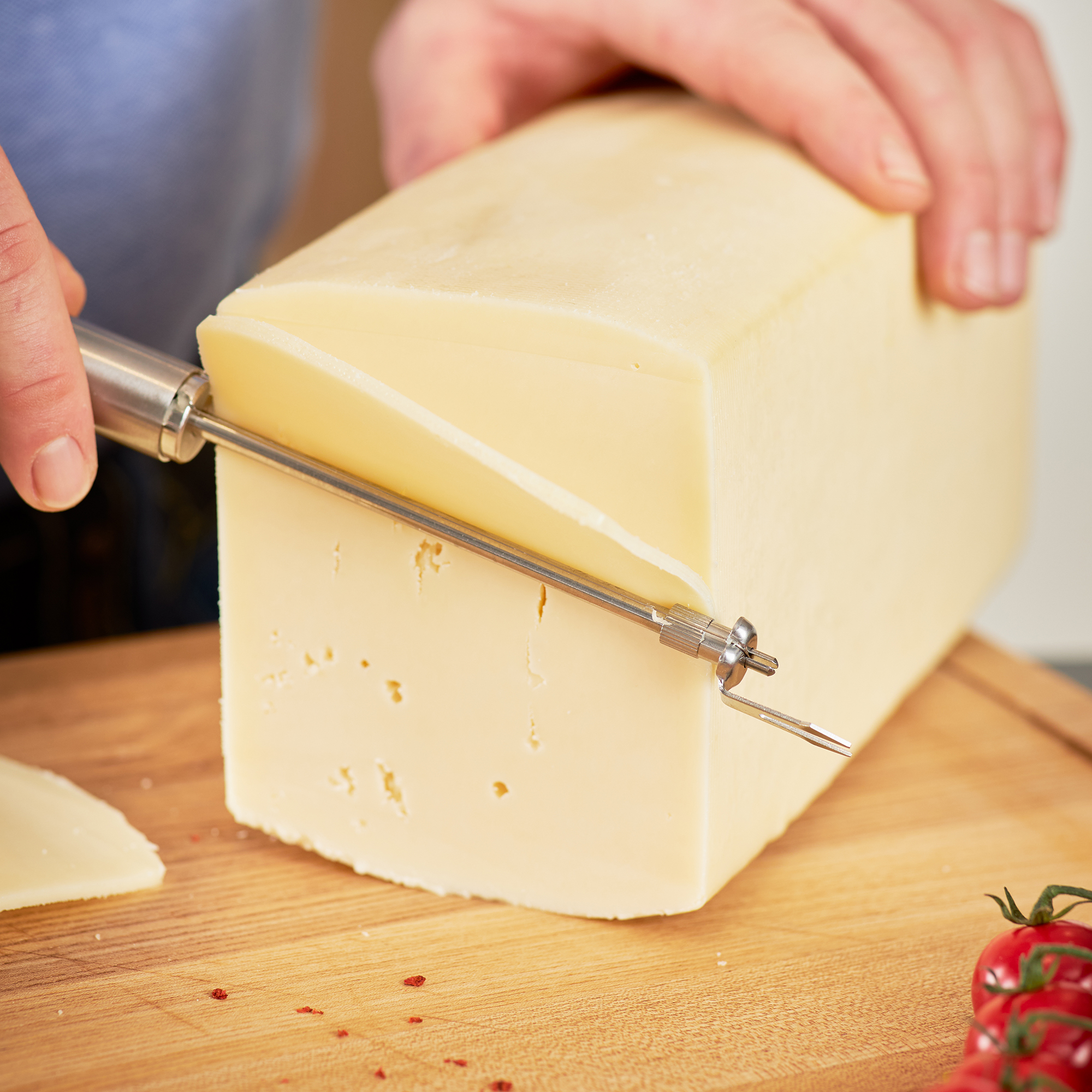 Wire cheese cutter from RÖSLE Wire cheese cutter cuts a piece of cheese on a wooden board.