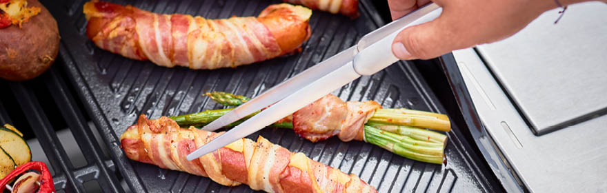 Grillgereedschap van RÖSLE op de grill Barbecueaccessoire met één hand die een barbecuegereedschap vasthoudt terwijl gegrild voedsel,...