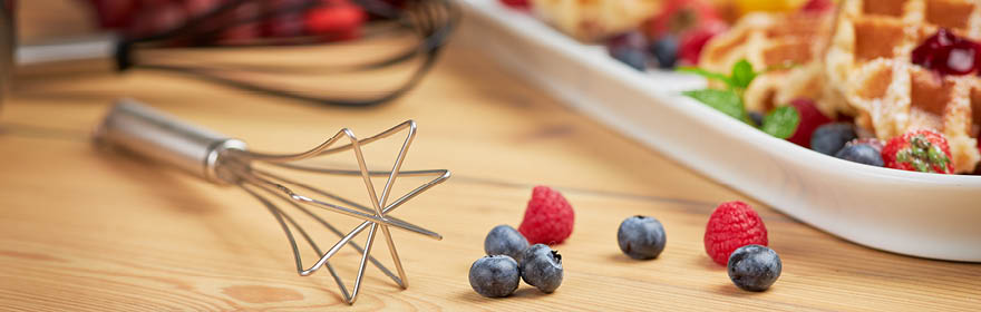 Roestvrijstalen garde met stervormig ontwerp, naast verse bessen en wafels op tafel.