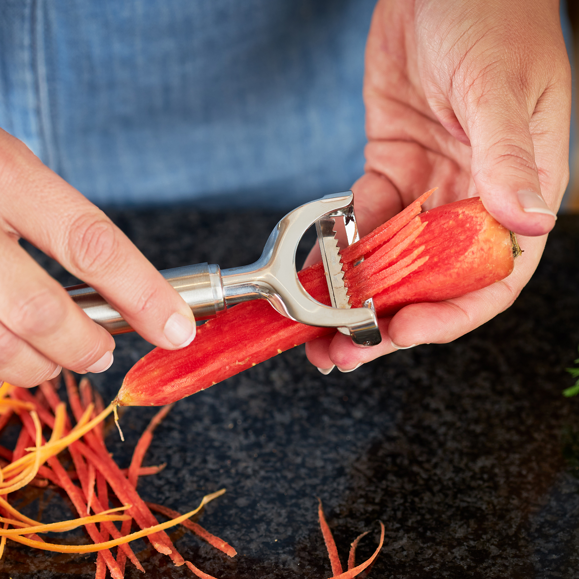 RÖSLE julienne peeler with carrot Julienne peeler in use while a person peels a carrot.