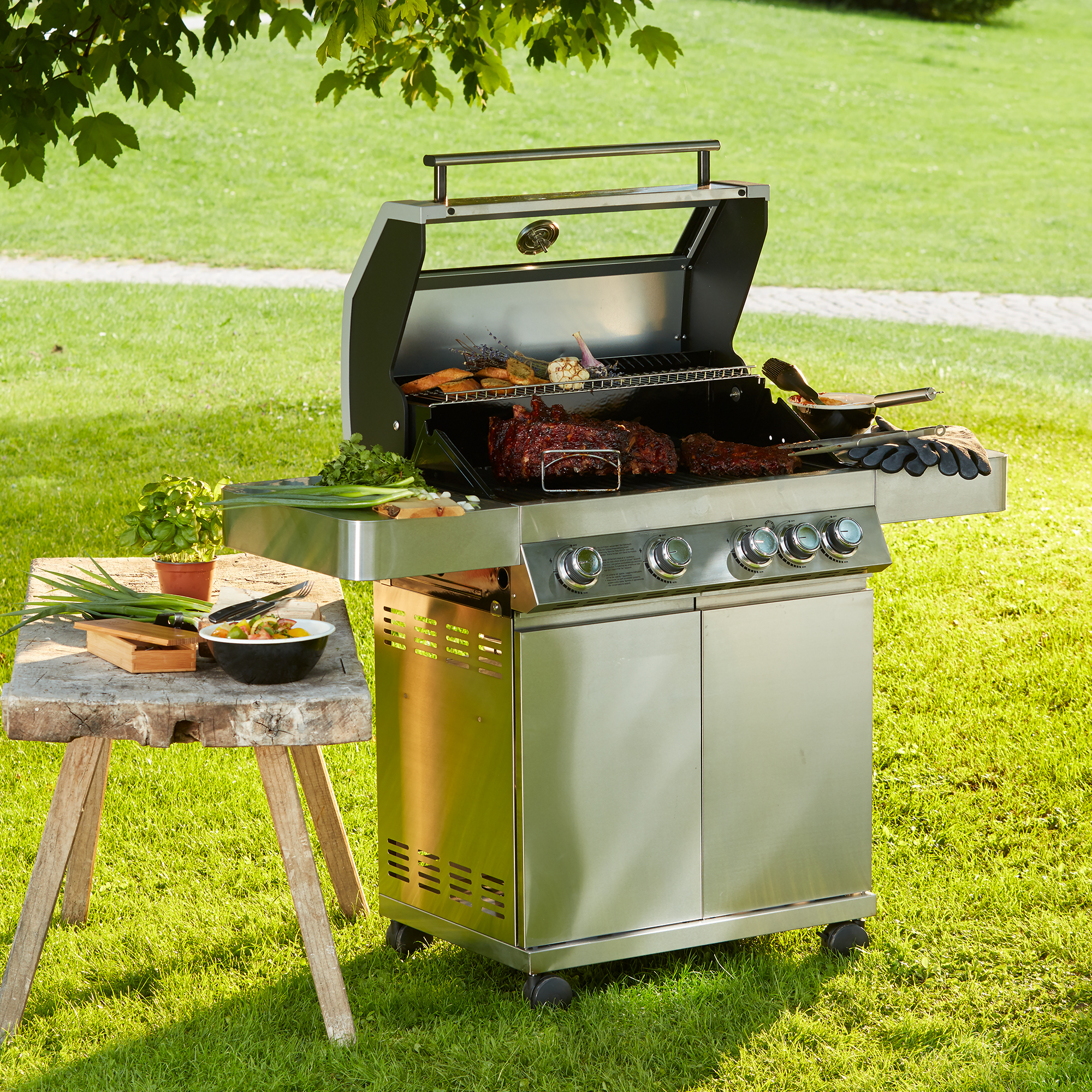 RÖSLE Gasgrill Videro G4 aus Edelstahl Gasgrill BBQ Station Videro G4 aus Edelstahl mit geöffnetem Deckel, Grillgut und Zubehör auf...