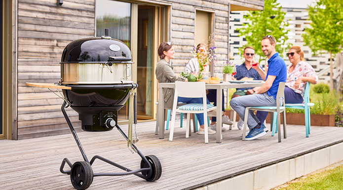 Charcoal kettle grill AIR F60 PRO with gourmet ring in the foreground and in the background friends sitting together at the table
