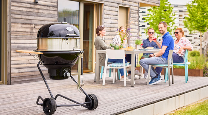 Holzkohle Kugelgrill AIR F60 PRO mit Gourmetring im Vordergrund und im Hintergrund sitzen Freunde zusammen am Tisch