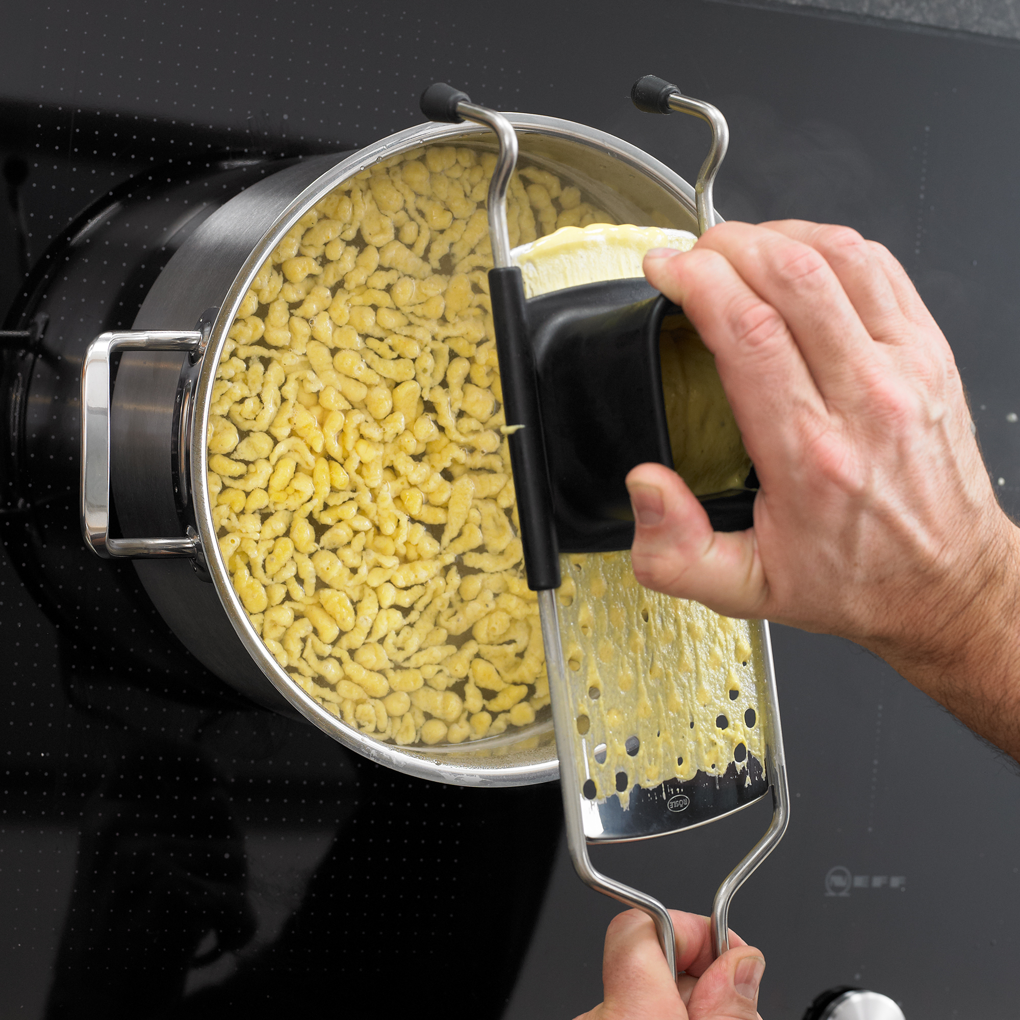 RÖSLE spaetzle slicer for preparing spaetzle Spaetzle slicer in use to press fresh spaetzle into a pot.