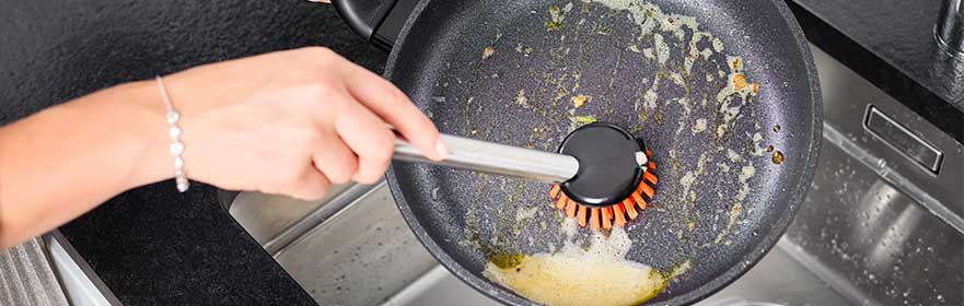 Keukenaccessoires schoonmaken Keukenaccessoires: Een pan schoonmaken met een speciale borstel.
