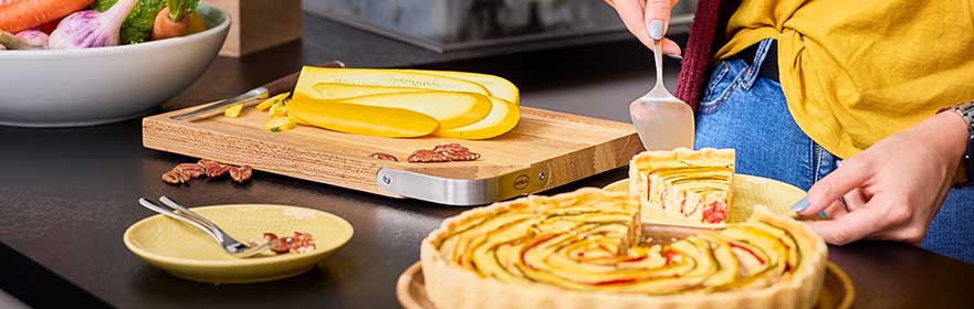 Serving Serving platter with a colourful cake and a person placing a piece of cake on a plate.