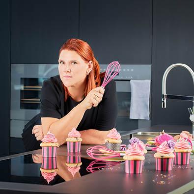 Woman holding the Pink Charity whisk with cupcakes in the kitchen