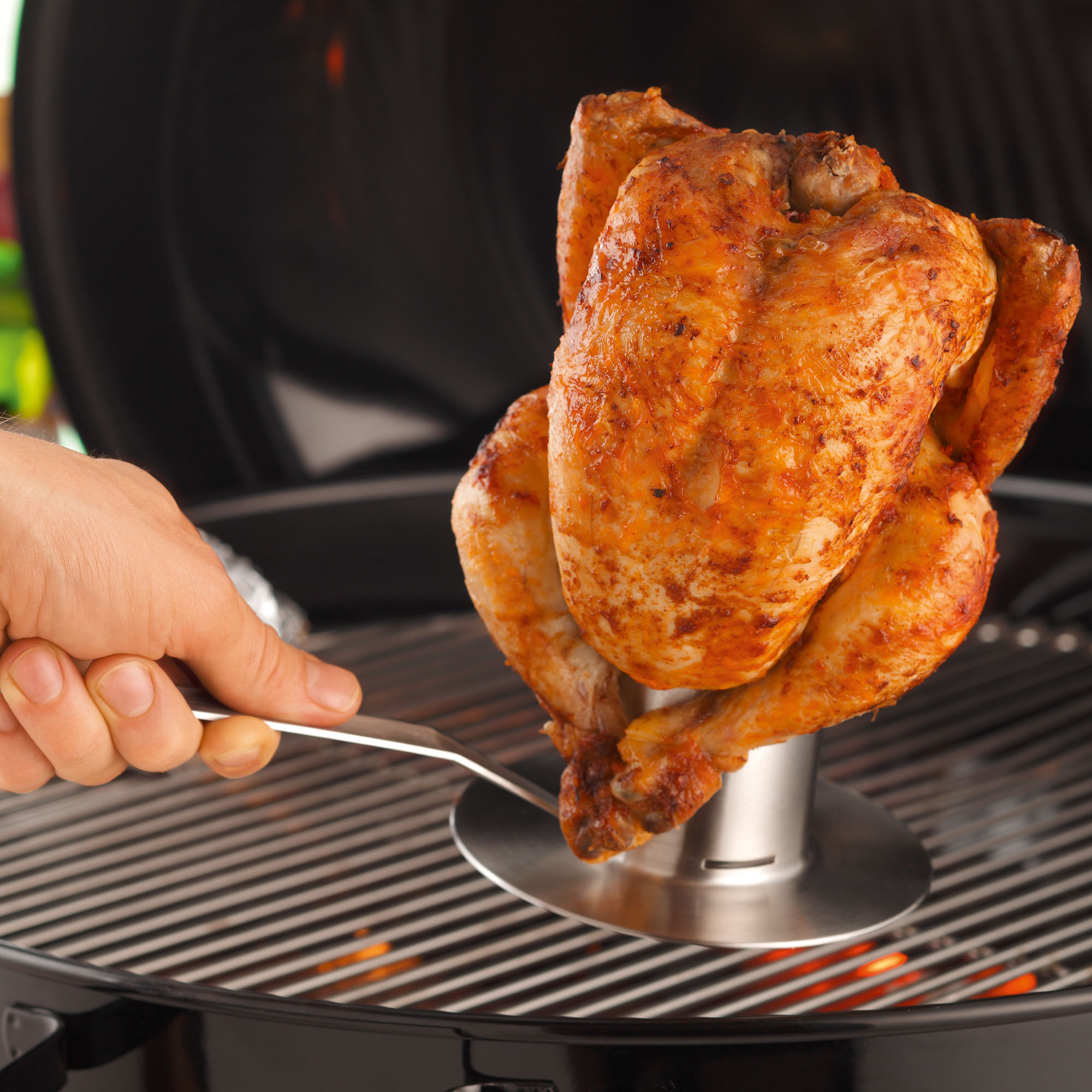 RÖSLE chicken roaster with grilled chicken Chicken roaster with a grilled chicken on a grill rack, hand holding tongs.