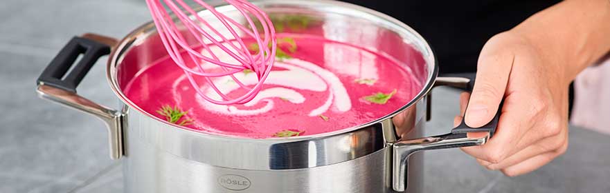 RÖSLE roestvrijstalen soeppot met roze soep Roestvrijstalen soeppot met roze soep en een garde.