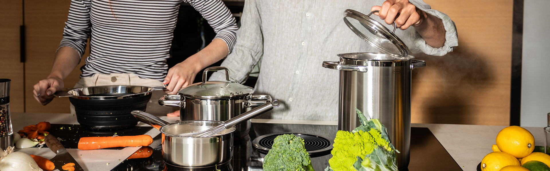 RÖSLE Suppentöpfe in einer modernen Küche Suppentöpfe aus Edelstahl auf einem Herd, während zwei Personen Gemüse zubereiten.