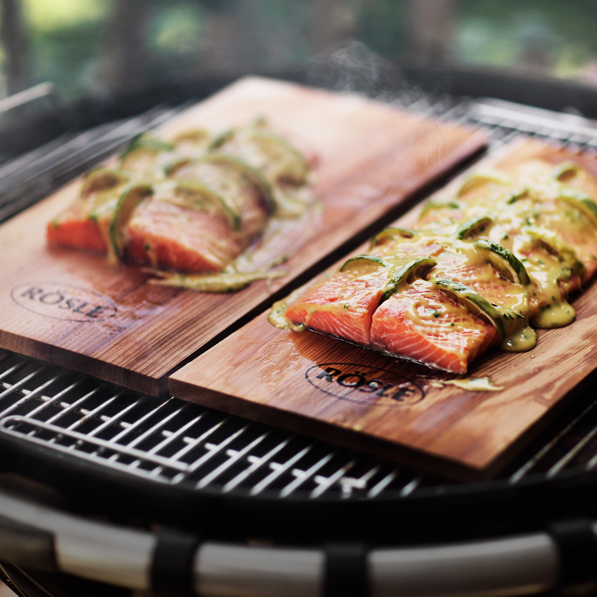 RÖSLE Zedernholz-Aromaplanken mit Lachsfilets Zedernholz-Aromaplanken im 2er-Set mit Lachsfilets und Gemüse auf einem Grill.
