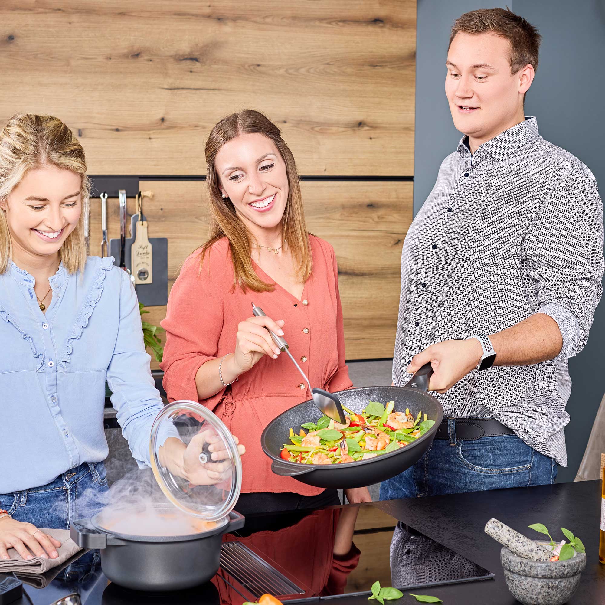 Kochszene in moderner Küche Drei Personen in einer modernen Küche, eine Person kocht mit einem Kochtopf, während die andere...