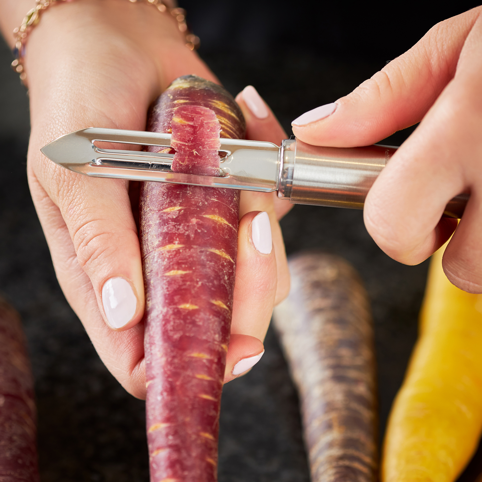 RÖSLE peeler with purple carrot Peeler in use, peeling a purple carrot, hand with manicure visible.