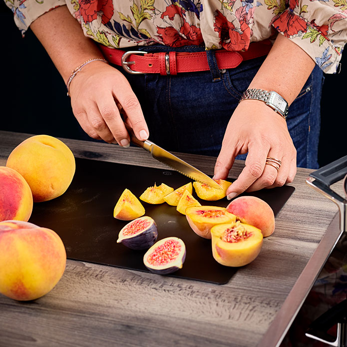 Frau schneidet Feigen und Pfirsiche auf Schneidbrett