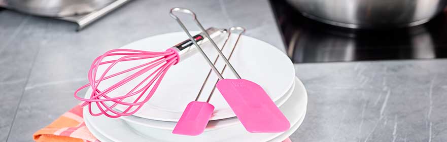 RÖSLE keukenaccessoires in roze Keukenaccessoires in roze: garde, spatel en tang op witte borden.