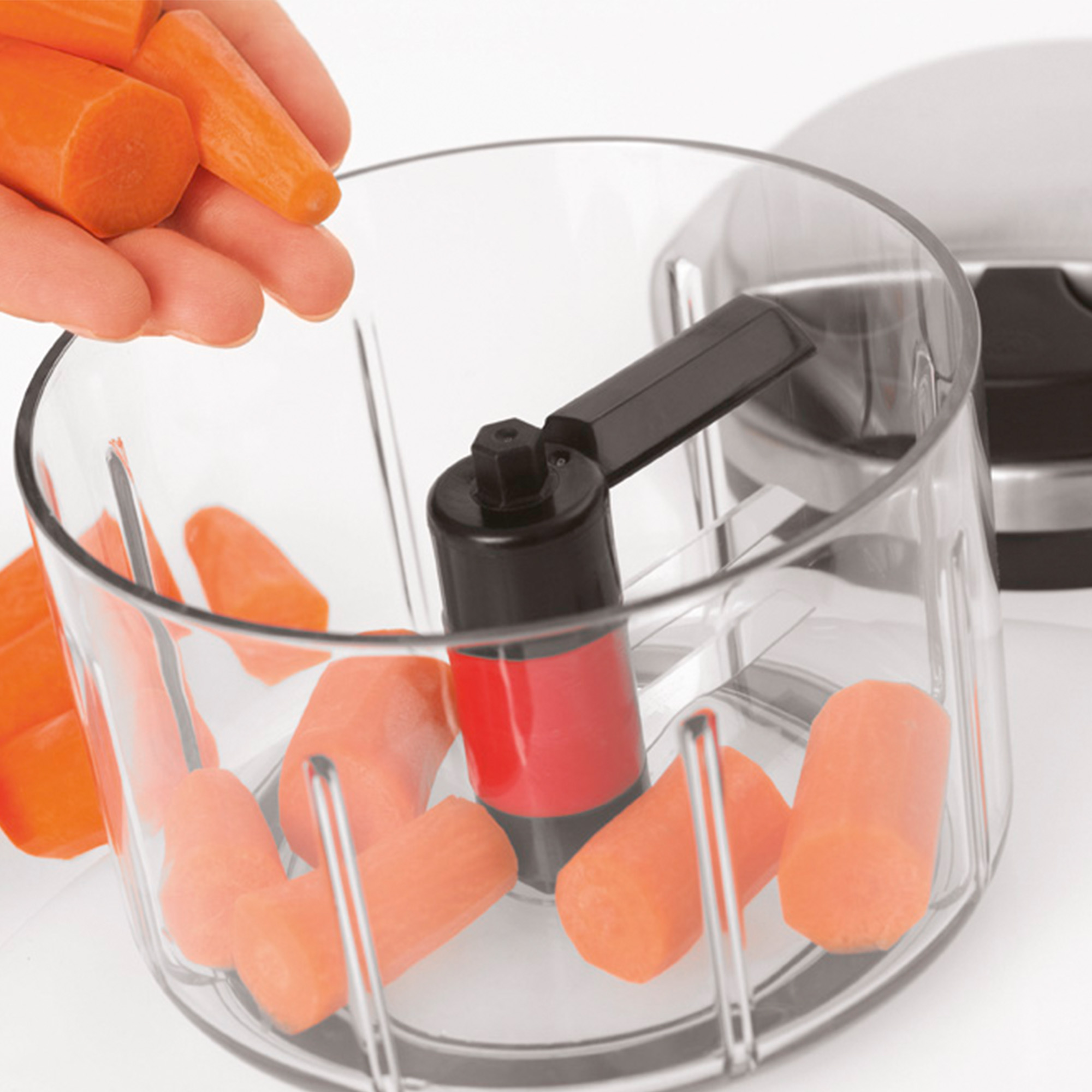RÖSLE Multischneider mit Karotten Multischneider mit transparentem Behälter und Karottenstücken, Hand greift nach Karotten.