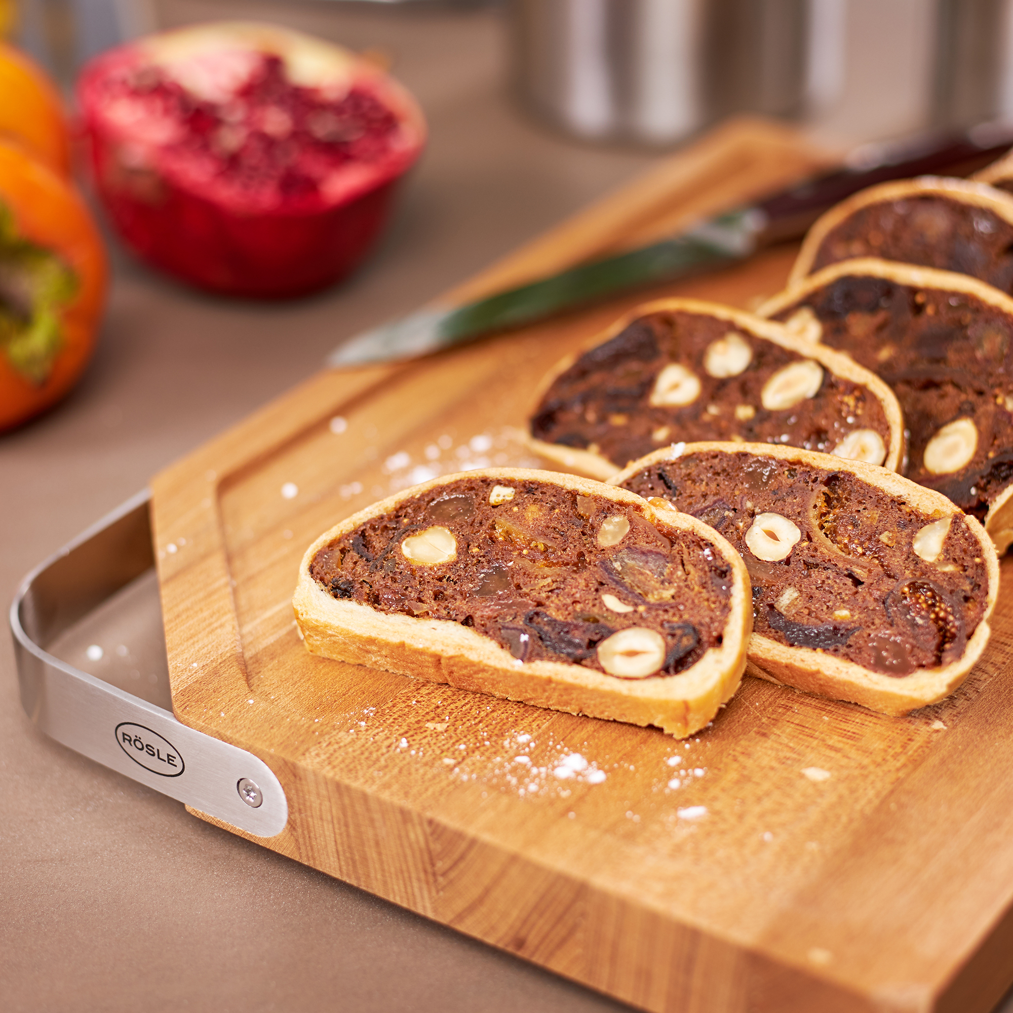 RÖSLE Holzschneidbrett mit Früchtebrot Schneidbrett aus Holz mit geschnittenem Früchtebrot und Nüssen, im Hintergrund Obst und eine...