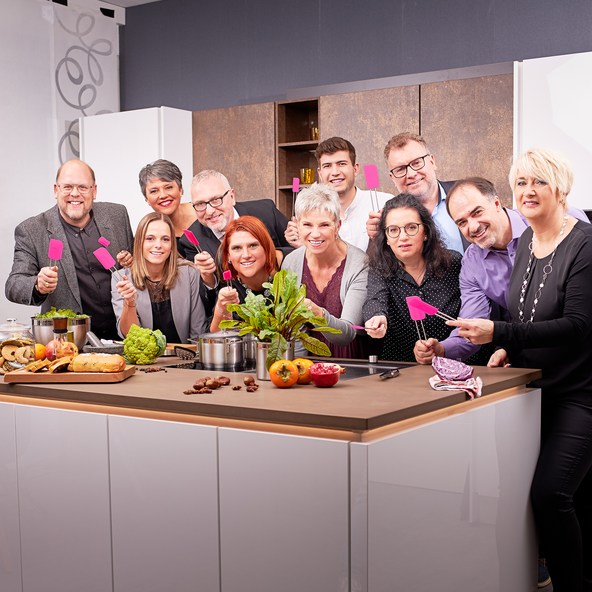 RÖSLE Teigschaber in einer Kochgruppe Gruppe von Personen in einer modernen Küche, die pinke Teigschaber halten, umgeben von frischen...