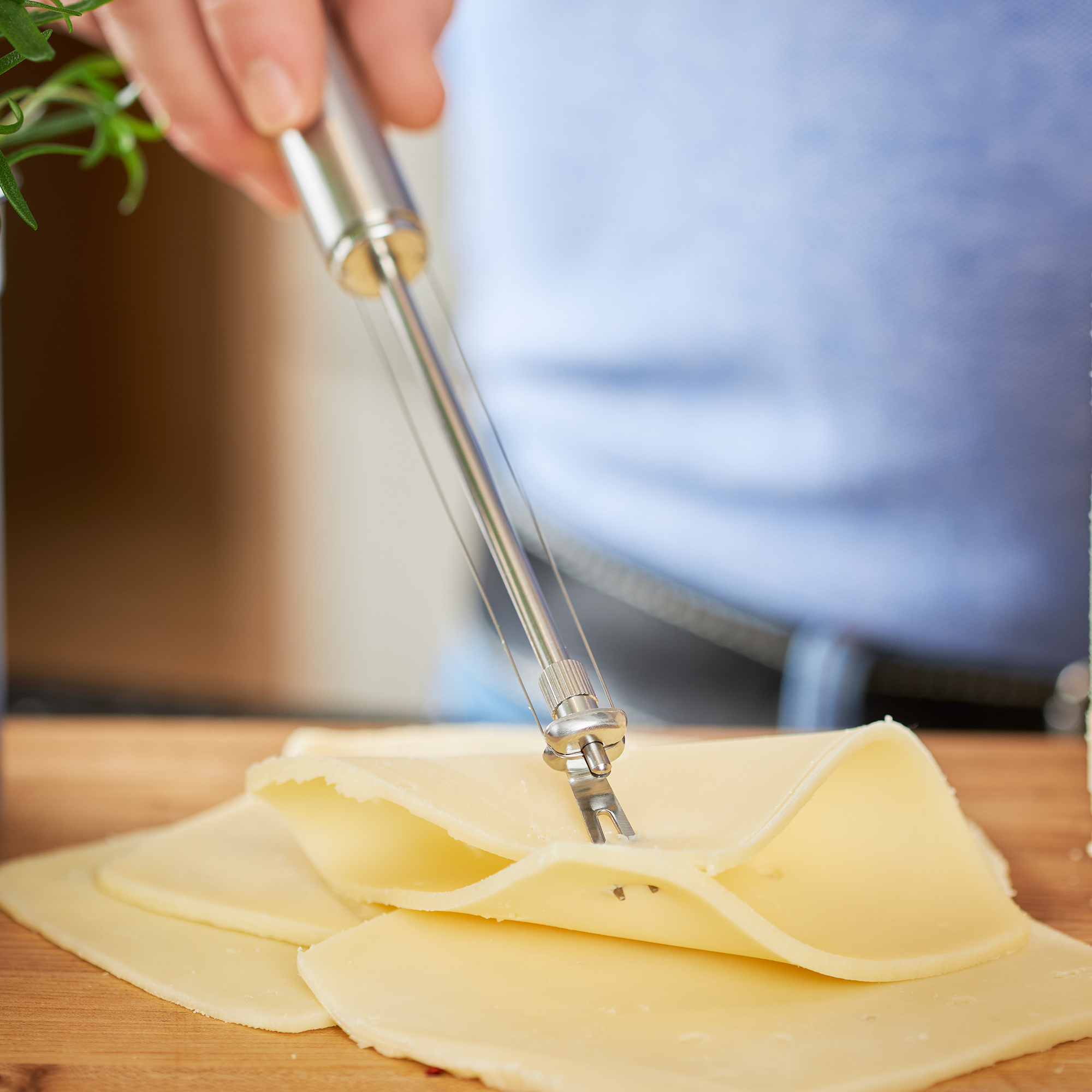 RÖSLE wire cheese cutter Wire cheese cutter made of stainless steel, held in the hand, cuts cheese on a wooden board.