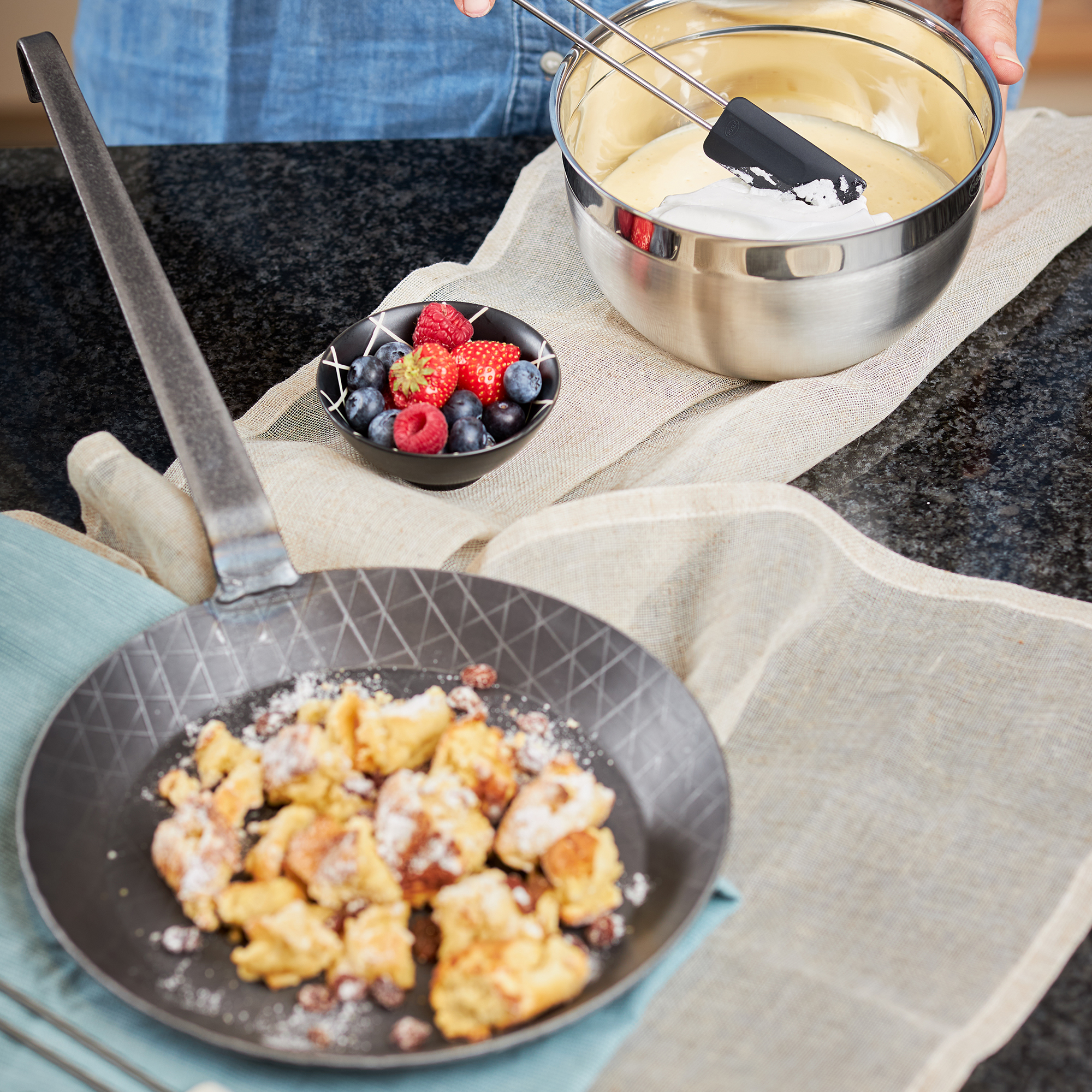 RÖSLE Schmiedeeisen Bratpfanne mit Teig und Beeren Bratpfanne aus Schmiedeeisen, 24 cm, mit gebratenem Teig und einer Schüssel mit Teig und Beeren.