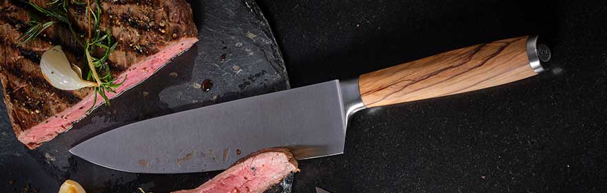 RÖSLE Artesano Kochmesser Artesano Kochmesser mit Holzgriff, auf einem schwarzen Untergrund neben geschnittenem Fleisch.