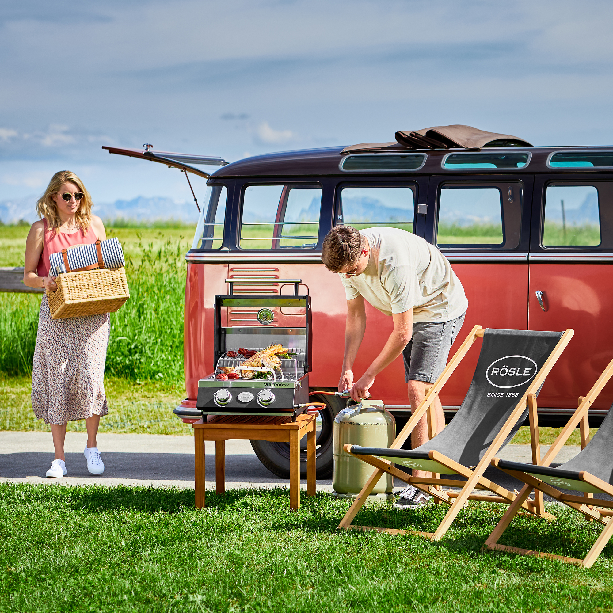 RÖSLE Gasgrill Videro G2-P im Freien Gasgrill Videro G2-P auf einem Tisch im Freien, während ein Mann grillt und eine Frau mit...