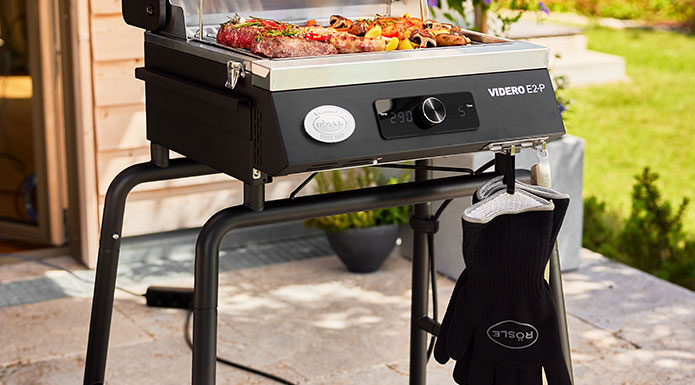 Elektrogrill E2-P Elektrogrill mit Untergestell auf der Terrasse. An dem Haken hängen Grillhandschuhe.