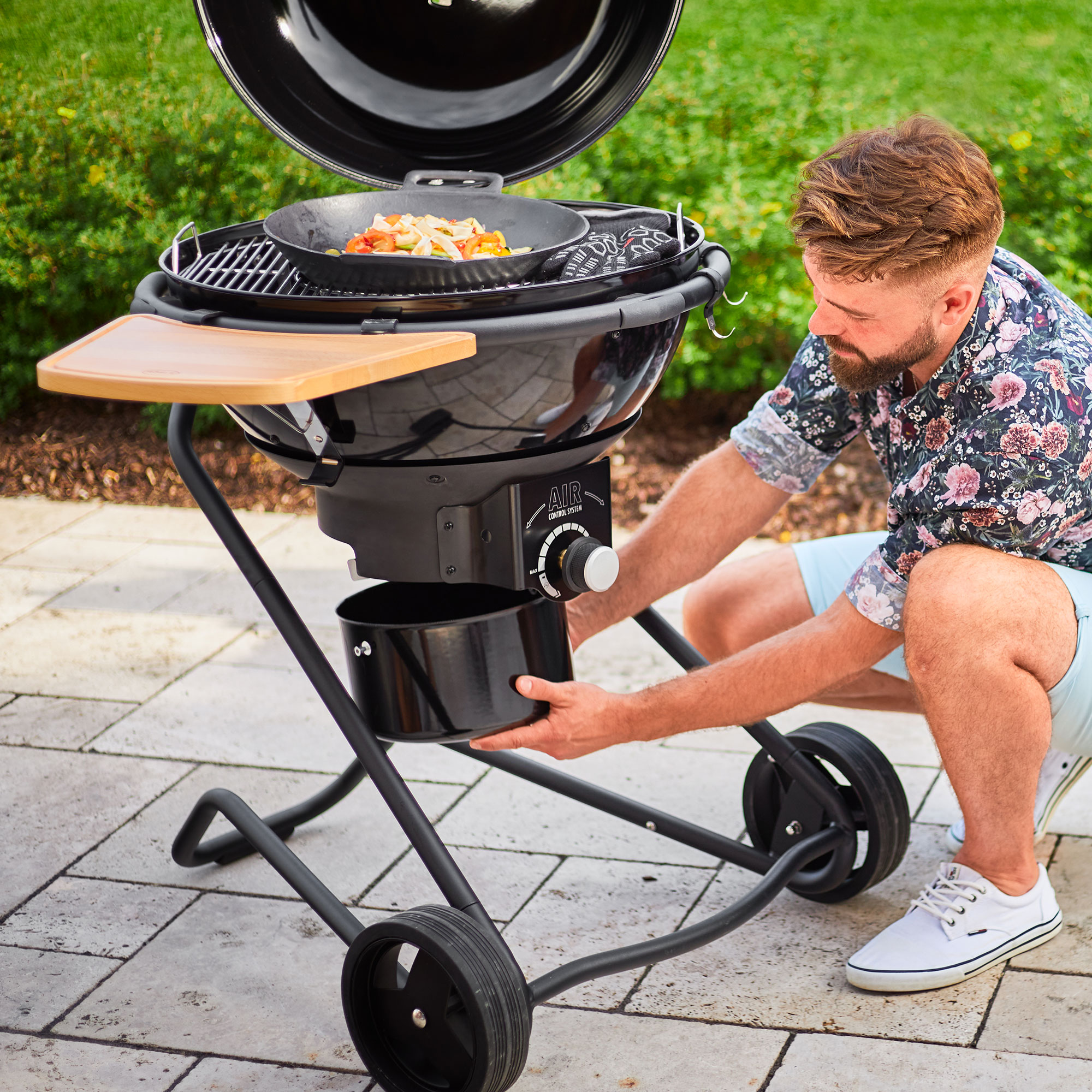 RÖSLE Holzkohle Kugelgrill No.1 AIR F60 PRO Holzkohle Kugelgrill No.1 AIR F60 PRO in Gebrauch, mit einem Mann, der den Aschebehälter entleert.