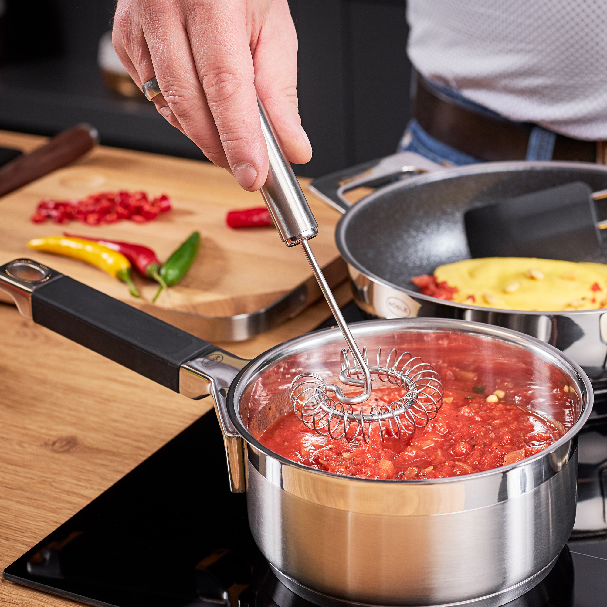 RÖSLE spiral broom in action Stainless steel spiral whisk, 22 cm, is used for stirring tomato sauce in a saucepan.