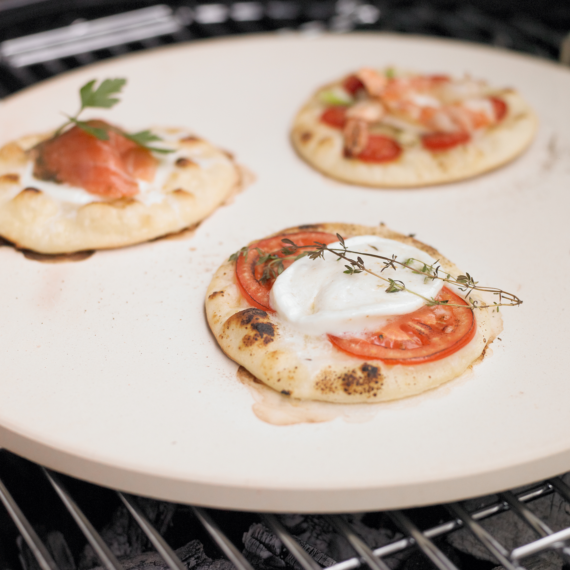 RÖSLE Pizzastein mit belegten Pizzen Pizzastein, rund, 41 cm, mit drei belegten Pizzen, darunter frische Tomaten, Kräuter und Schinken.