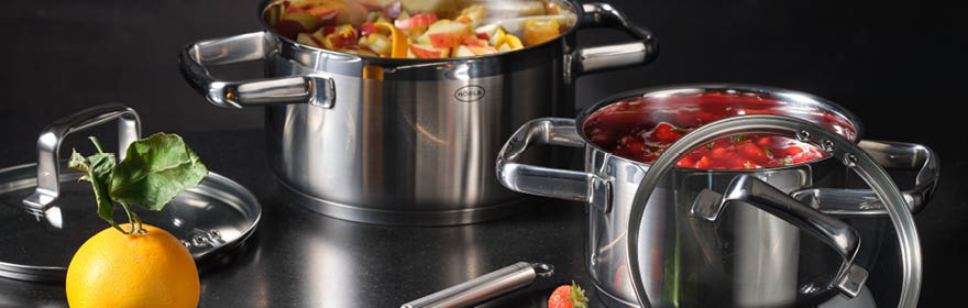 Cookware Stainless steel cooking pots with lids, one filled with pieces of fruit, the other with red...