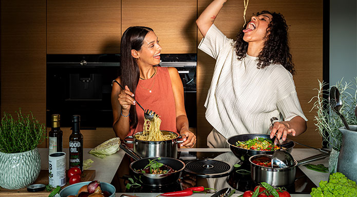 Pureelements Zwei Frauen kochen zusammen und essen Spaghetti mit der Hand.