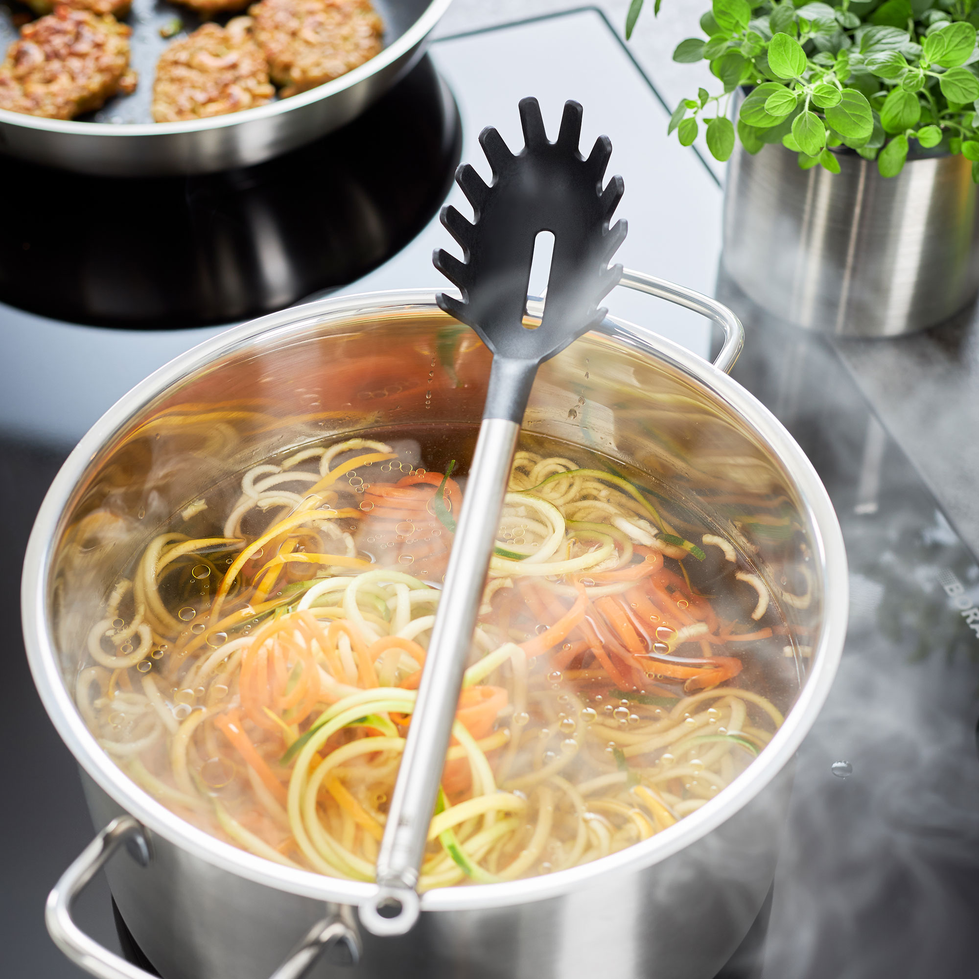 RÖSLE Gourmet Set Pasta Gourmet Set mit einem schwarzen Spaghettiheber in einem Topf mit dampfender Pasta und Gemüse.